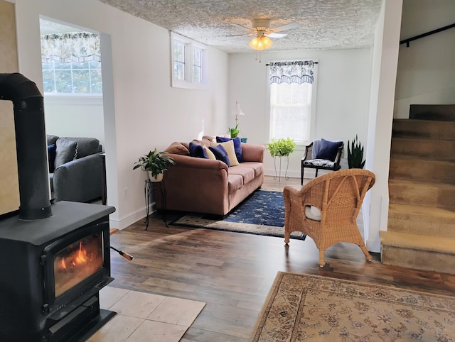 living room featuring ceiling fan, light hardwood / wood-style floors, a textured ceiling, and a wood stove