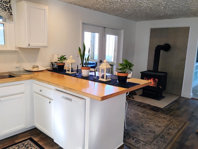 kitchen featuring white cabinetry, a wood stove, white dishwasher, and kitchen peninsula