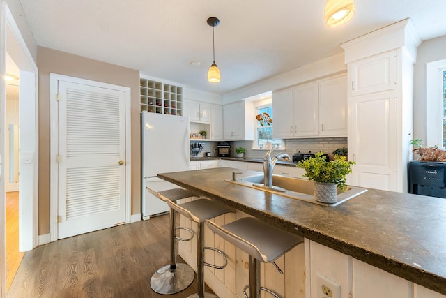 kitchen with pendant lighting, white cabinets, a kitchen breakfast bar, white refrigerator, and dark wood-type flooring