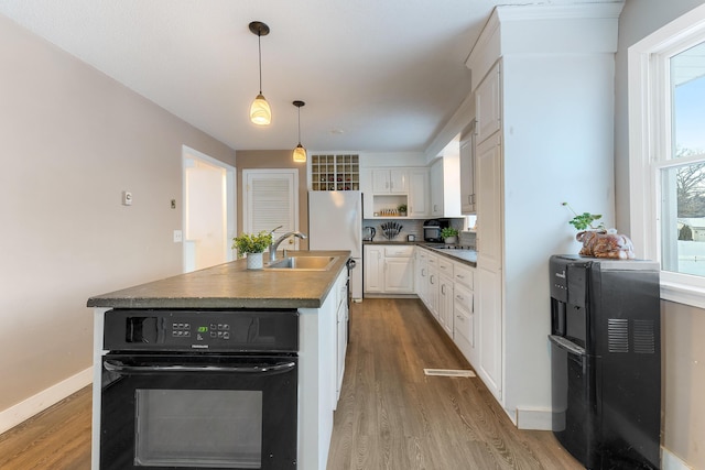 kitchen featuring decorative light fixtures, white cabinetry, oven, hardwood / wood-style flooring, and a center island with sink