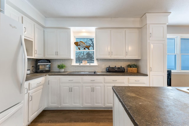 kitchen featuring dark wood-type flooring, white fridge, dark stone counters, decorative backsplash, and white cabinets