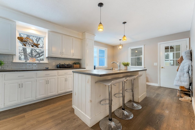 kitchen with pendant lighting, a breakfast bar, dark hardwood / wood-style floors, white cabinets, and a center island with sink