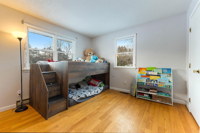 bedroom with multiple windows, a baseboard radiator, a textured ceiling, and light hardwood / wood-style floors