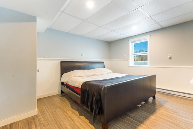 bedroom with a drop ceiling, light hardwood / wood-style flooring, and a baseboard radiator