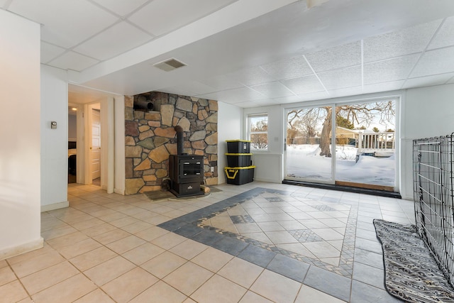 unfurnished living room featuring a wood stove, light tile patterned floors, and a drop ceiling