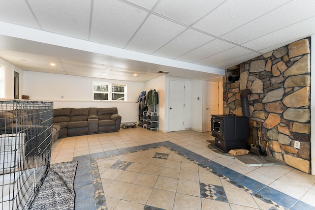 unfurnished living room with a paneled ceiling, a wood stove, and light tile patterned flooring