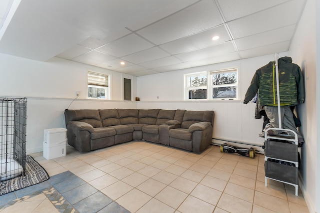 living room with light tile patterned floors, a wealth of natural light, a paneled ceiling, and a baseboard heating unit