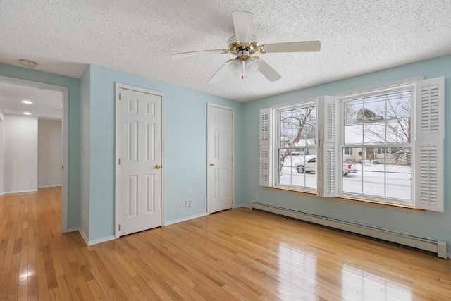 unfurnished bedroom featuring a baseboard heating unit, ceiling fan, multiple closets, a textured ceiling, and light hardwood / wood-style flooring