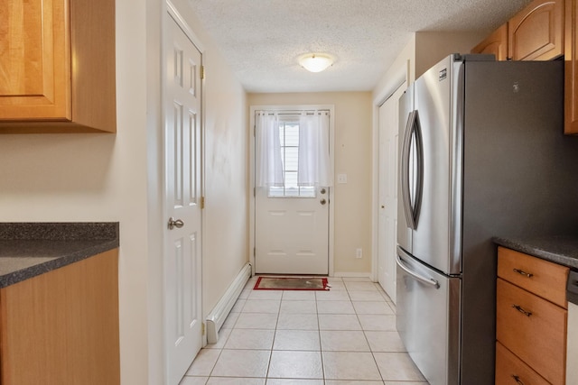 kitchen featuring light tile patterned floors, a textured ceiling, stainless steel refrigerator, and baseboard heating