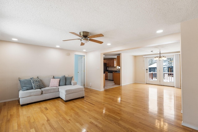 unfurnished living room featuring ceiling fan with notable chandelier, light hardwood / wood-style flooring, and a textured ceiling