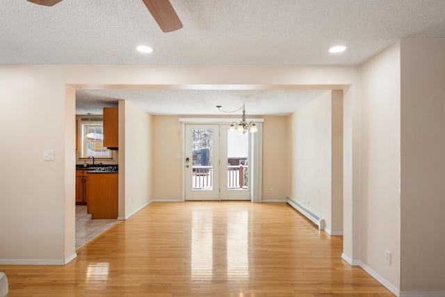 unfurnished room featuring sink, a textured ceiling, ceiling fan with notable chandelier, a baseboard radiator, and light wood-type flooring