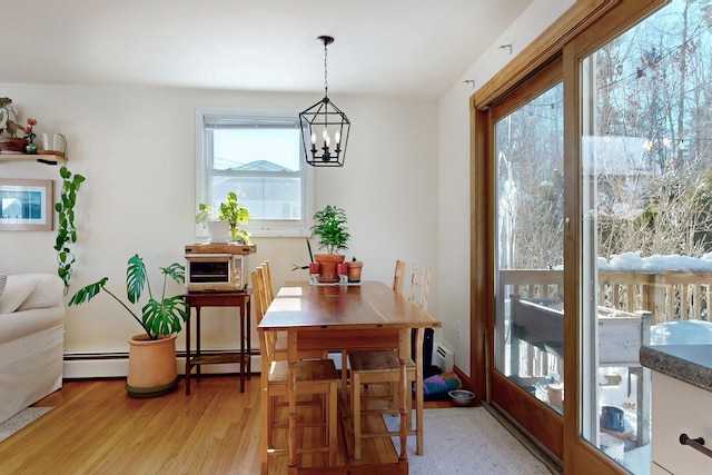 dining area featuring a baseboard heating unit, light wood-style flooring, and a notable chandelier