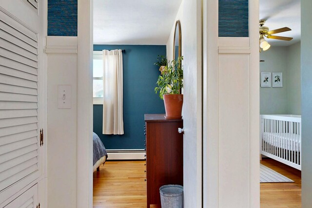 bedroom with a crib, baseboards, a baseboard heating unit, and wood finished floors