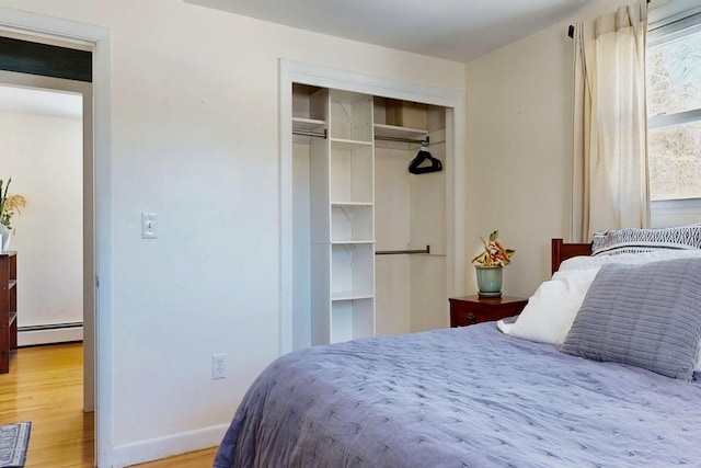 bedroom featuring a closet, baseboards, baseboard heating, and wood finished floors