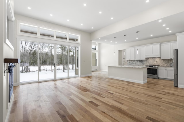 kitchen with pendant lighting, white cabinetry, sink, stainless steel appliances, and a center island with sink