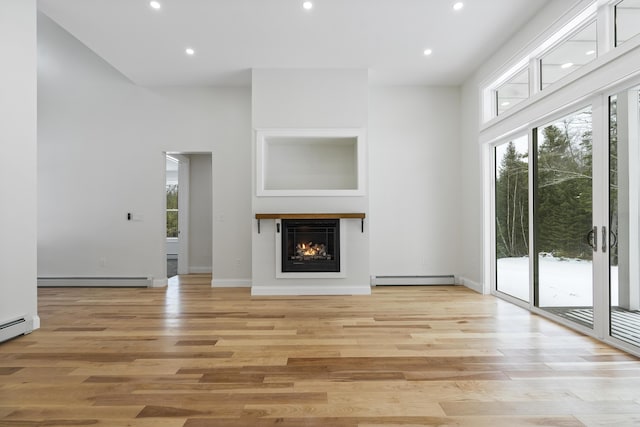 unfurnished living room with a baseboard radiator, a wealth of natural light, and light wood-type flooring