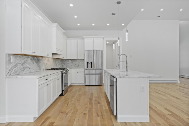 kitchen with white cabinetry, light stone counters, hanging light fixtures, stainless steel appliances, and a kitchen island with sink