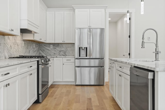 kitchen featuring decorative light fixtures, light hardwood / wood-style flooring, appliances with stainless steel finishes, light stone countertops, and white cabinets