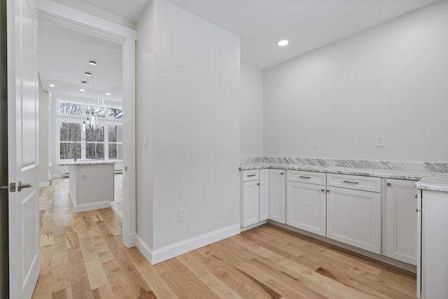 interior space featuring white cabinetry, light stone countertops, pendant lighting, and light hardwood / wood-style flooring