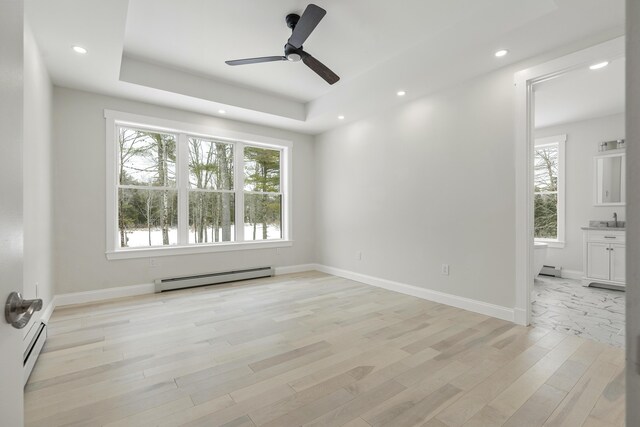 spare room featuring a baseboard heating unit, light hardwood / wood-style floors, and a tray ceiling