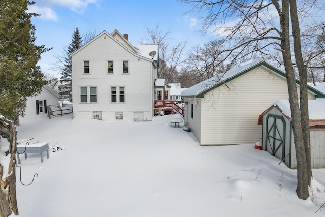 snow covered property with an outbuilding, a shed, and a chimney