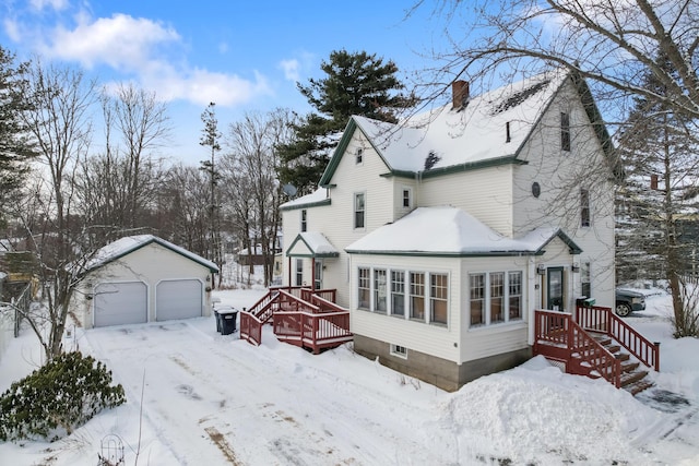 view of snowy exterior featuring a garage, an outbuilding, and a chimney