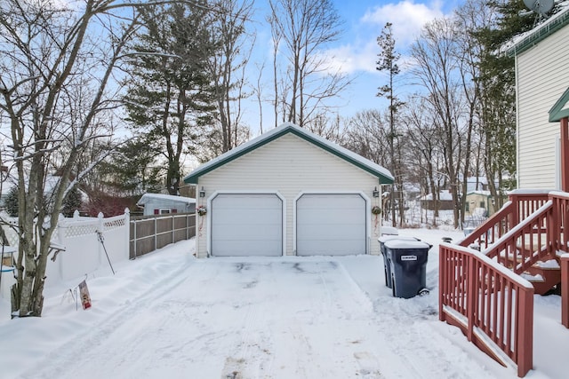 snow covered garage featuring a garage and fence