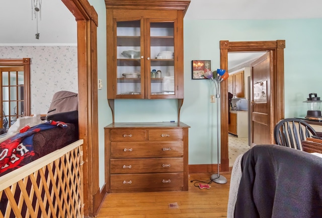 interior space featuring crown molding, light wood-style flooring, baseboards, and wallpapered walls