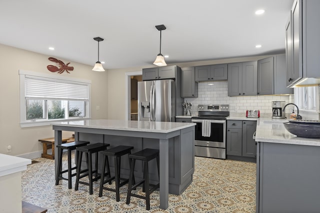 kitchen with a center island, gray cabinets, pendant lighting, stainless steel appliances, and backsplash