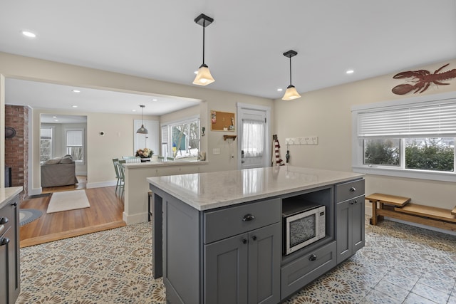 kitchen with gray cabinets, a kitchen island, light stone counters, and decorative light fixtures