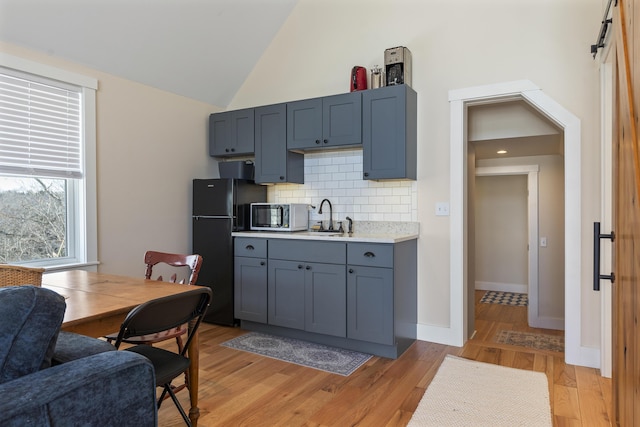 kitchen with lofted ceiling, sink, light hardwood / wood-style flooring, and black fridge