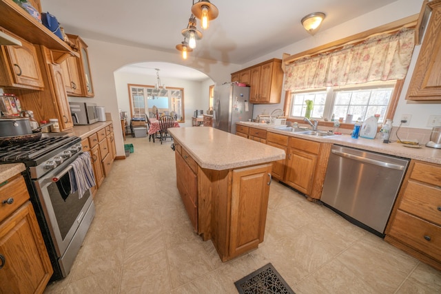 kitchen featuring appliances with stainless steel finishes, a center island, sink, and decorative light fixtures