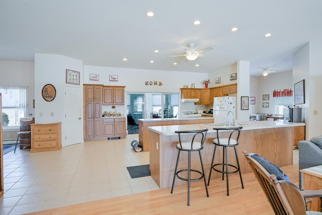 kitchen featuring white fridge, stove, a large island with sink, a kitchen breakfast bar, and ceiling fan