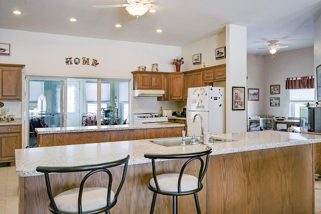 kitchen with a breakfast bar, a spacious island, light stone countertops, white refrigerator, and sink