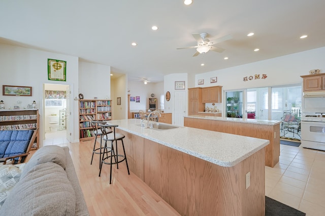 kitchen featuring an island with sink, light stone counters, white range with gas stovetop, sink, and a kitchen bar