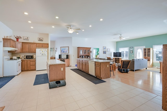 kitchen with white appliances, a breakfast bar, sink, ceiling fan, and a kitchen island with sink