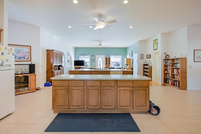 kitchen with light tile patterned floors, light stone countertops, white fridge, sink, and kitchen peninsula