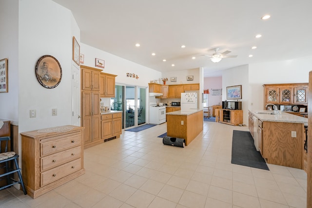 kitchen featuring white appliances, light stone counters, ceiling fan, sink, and a kitchen island with sink