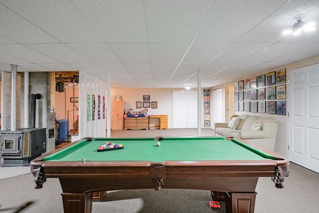 rec room with a wood stove, a paneled ceiling, and carpet floors