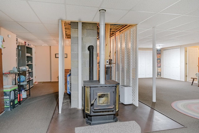 basement with a wood stove and a paneled ceiling