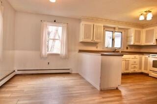 kitchen featuring white cabinetry, a baseboard radiator, sink, range, and light hardwood / wood-style flooring