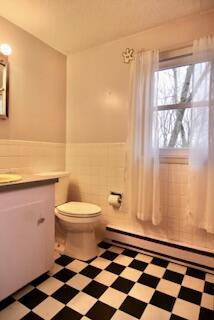 bathroom featuring baseboard heating, vanity, toilet, and tile walls