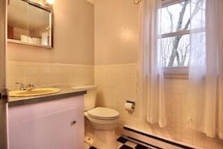 bathroom featuring vanity, toilet, tile walls, and a baseboard heating unit