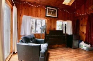 sitting room with wooden walls, light hardwood / wood-style floors, and vaulted ceiling with skylight