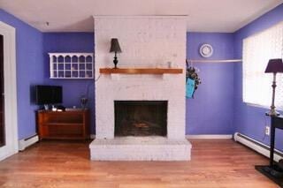 living room featuring a baseboard heating unit, hardwood / wood-style floors, and a fireplace