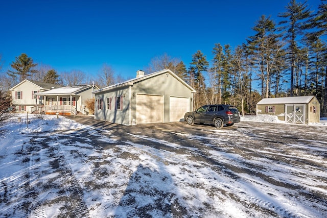 view of snowy exterior featuring a porch, a storage unit, and a garage