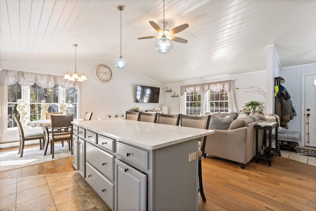 kitchen with lofted ceiling, gray cabinetry, a center island, light wood-type flooring, and a kitchen breakfast bar