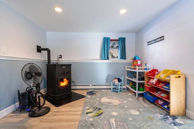 playroom featuring wood-type flooring, a baseboard radiator, and a wood stove