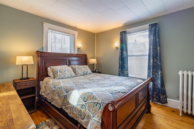 bedroom featuring multiple windows, radiator heating unit, and light hardwood / wood-style floors