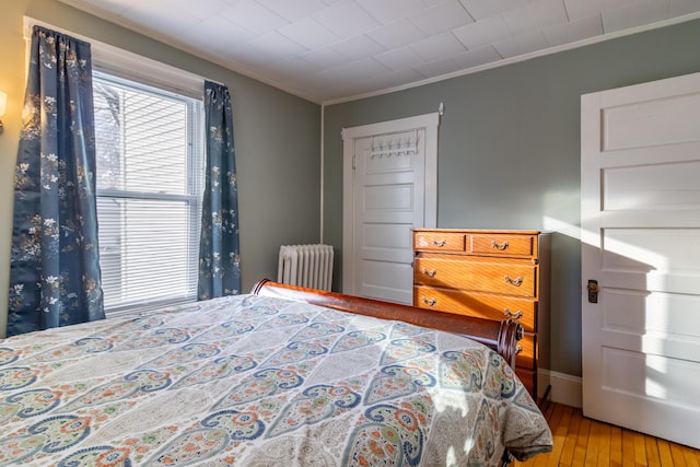 bedroom featuring hardwood / wood-style floors, radiator heating unit, and ornamental molding